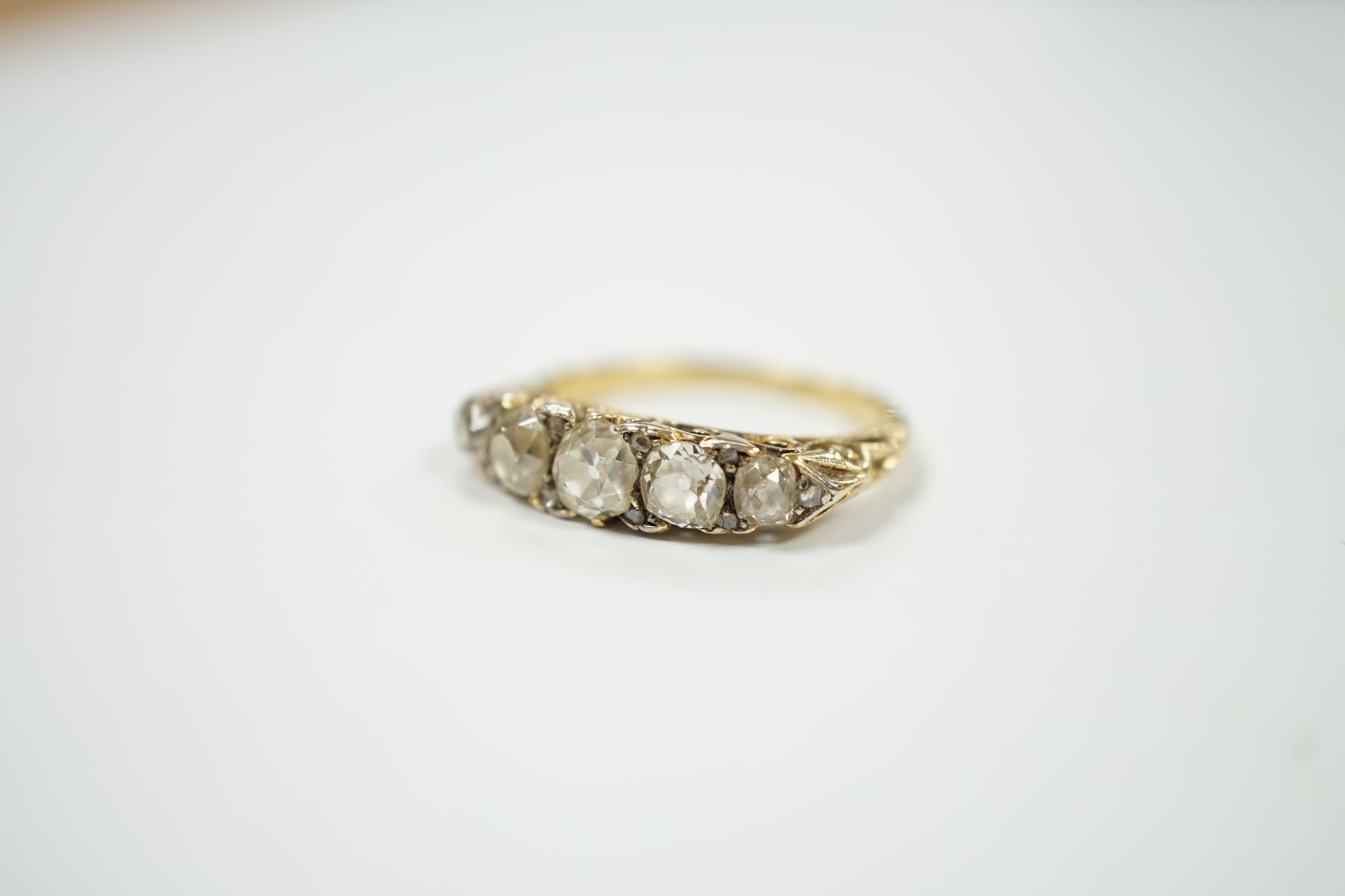 An early 20th century yellow metal and graduated five stone diamond set half hoop ring, with diamond chip spacers, size N/O, gross weight 4.7 grams.